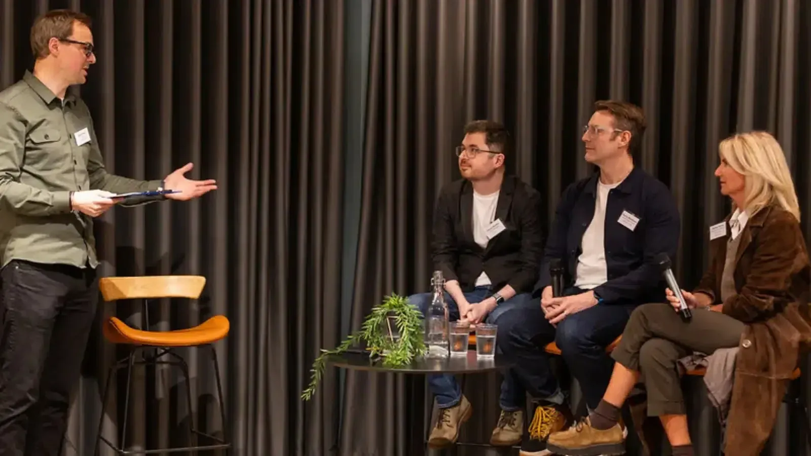 A host introducing a panel of three speakers at a Prolific North event