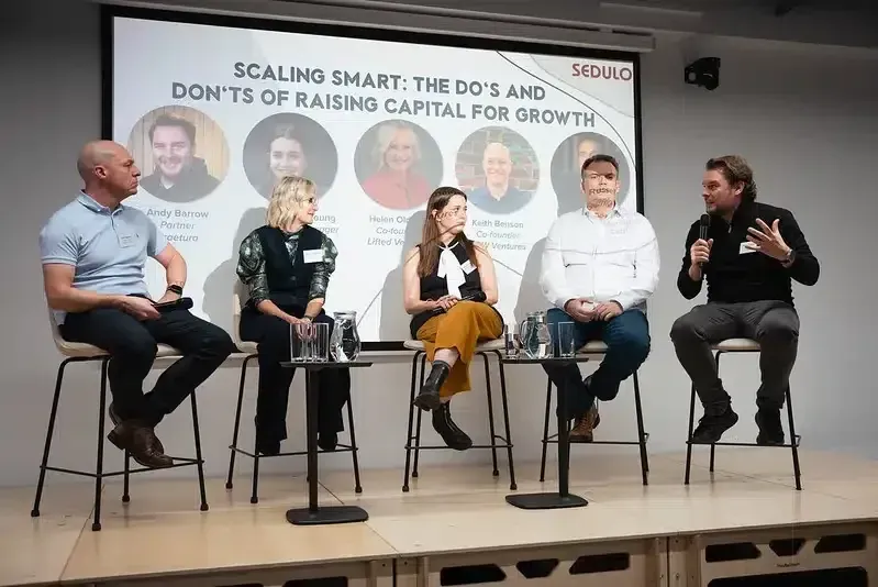 A panel of five speakers on stage in front of a presentation screen
